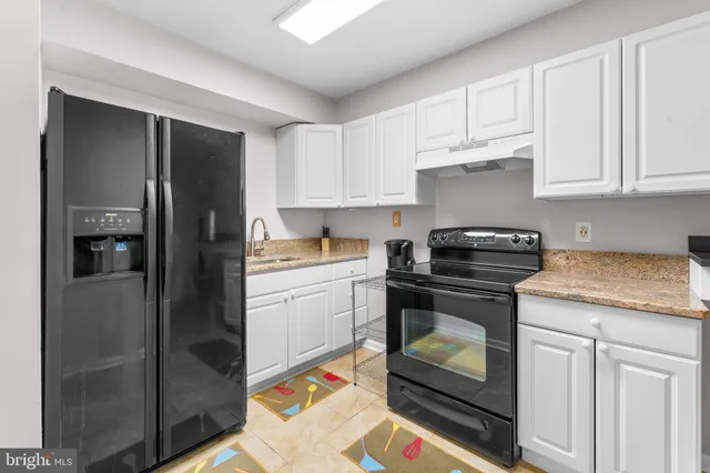 a kitchen with granite countertop a refrigerator stove and white cabinets