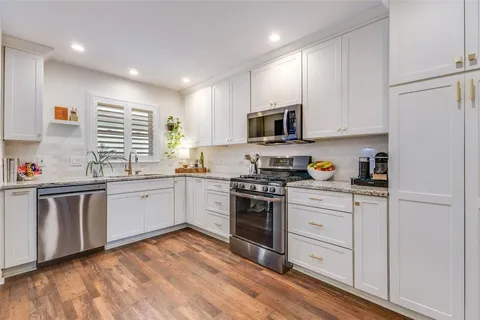 a kitchen with stainless steel appliances granite countertop white cabinets a sink a stove a refrigerator and microwave with wooden floor