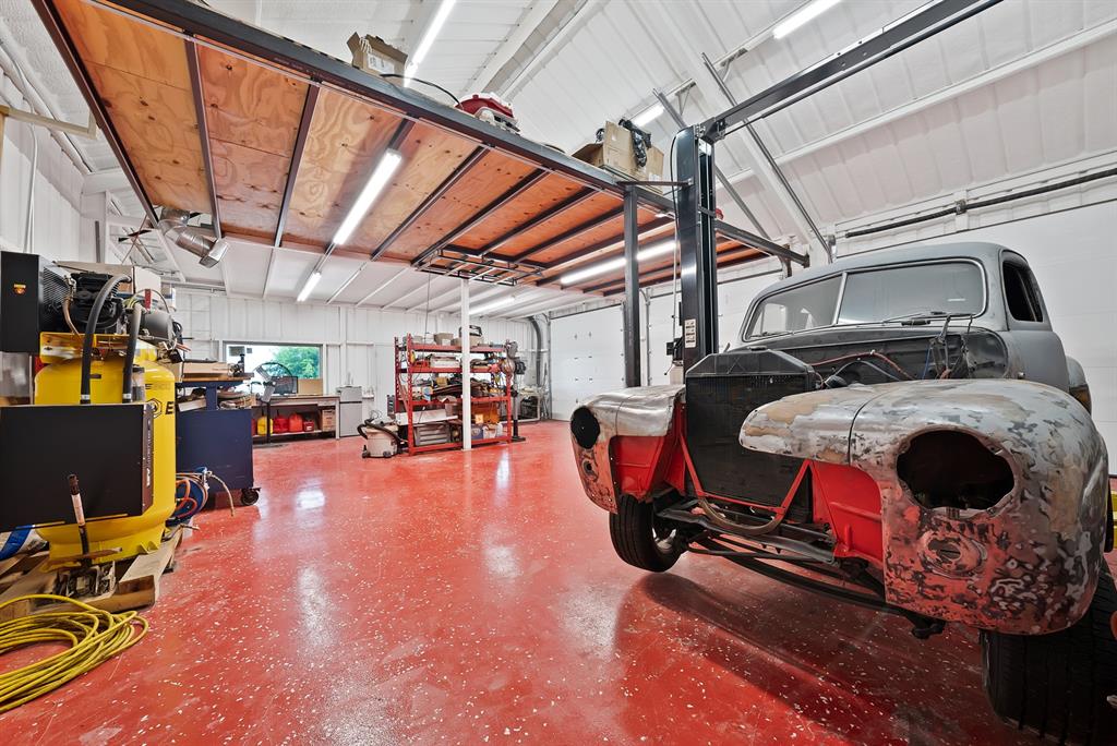 100 Shadle Ridge Court Poolville, TX 76487 - Photo 34 of 40 Spacious workshop featuring a high vaulted ceiling, red speckled flooring, ample fluorescent lighting, and a vehicle lift system