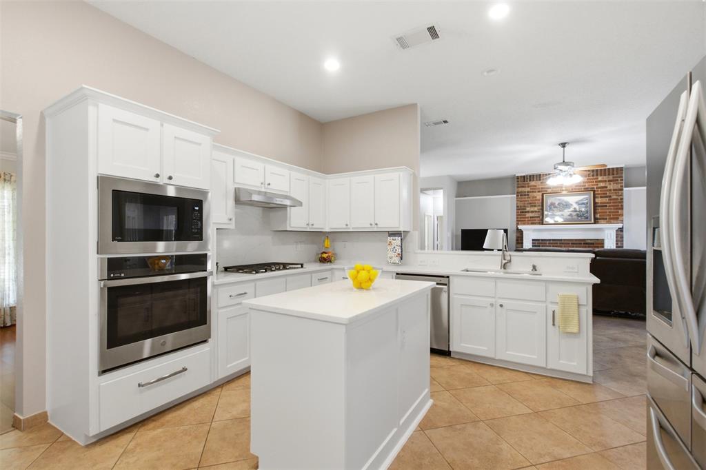 4218 Glistening Spring Rowlett, TX 75088 - Photo 13 of 39 Bright kitchen featuring white cabinetry, a built-in stainless steel microwave and oven, a gas range with a stainless steel vent hood, and a central island with a solid surface countertop
