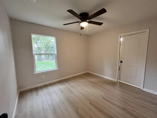 an empty room with wooden floor fan and windows