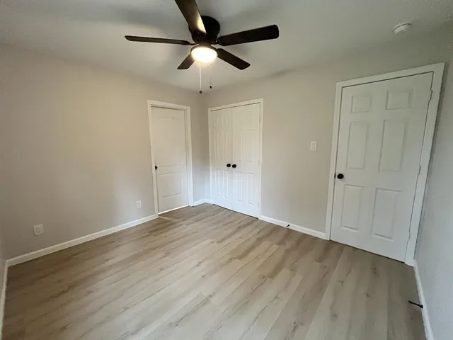 an empty room with wooden floor ceiling fan and windows