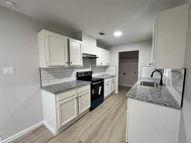 a kitchen with stainless steel appliances granite countertop a sink dishwasher a stove top oven a refrigerator with white cabinets and wooden floor