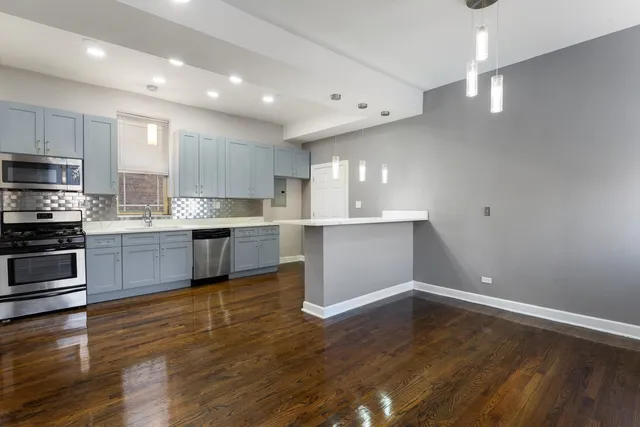 a kitchen with stainless steel appliances kitchen island granite countertop a stove a sink and white cabinets with wooden floor