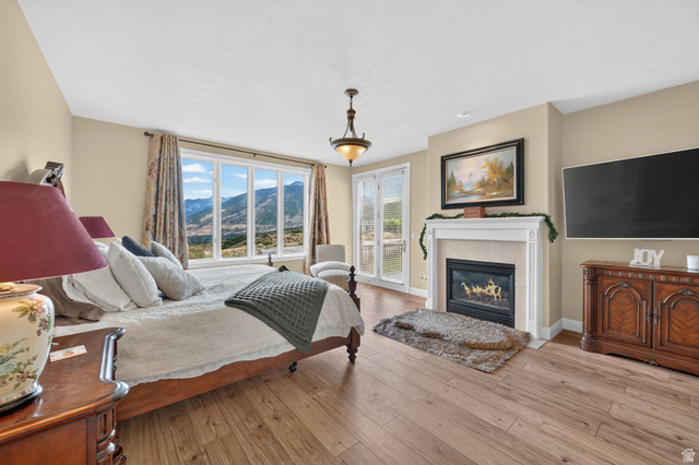 767 Draper View Road Draper, UT 84020 - Photo 24 of 71 Spacious room featuring wood-finish flooring, a large multi-pane window with mountain scenery, a white-mantled fireplace with a light-toned surround, a ceiling-mounted light fixture, and double glass doors opening to the exterior
