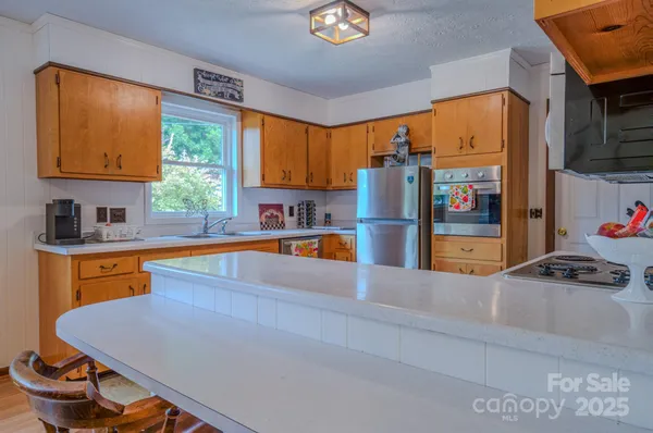 a kitchen with stainless steel appliances granite countertop a refrigerator a sink dishwasher a stove and a dining table with wooden floor