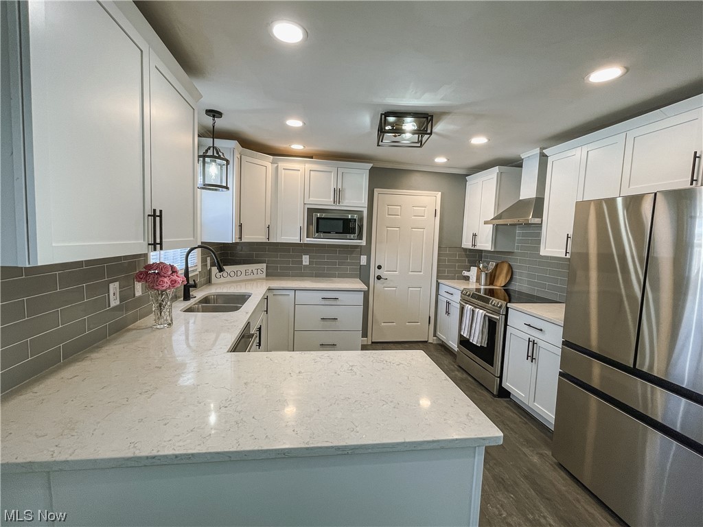 24709 Emery Road Warrensville Heights, OH 44128 - Photo 10 of 34 Kitchen with hanging light fixtures, tasteful backsplash, dark hardwood / wood-style flooring, appliances with stainless steel finishes, and wall chimney range hood