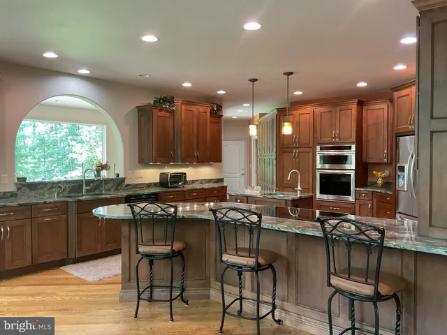 a kitchen with stainless steel appliances granite countertop a refrigerator a stove and a sink with wooden cabinets