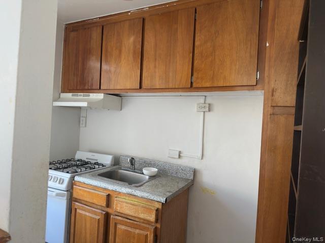 1332 Metropolitan Avenue, Unit 6A Bronx, NY 10462 - Photo 9 of 11 Kitchen with white range with gas cooktop, brown cabinetry, under cabinet range hood, and light countertops