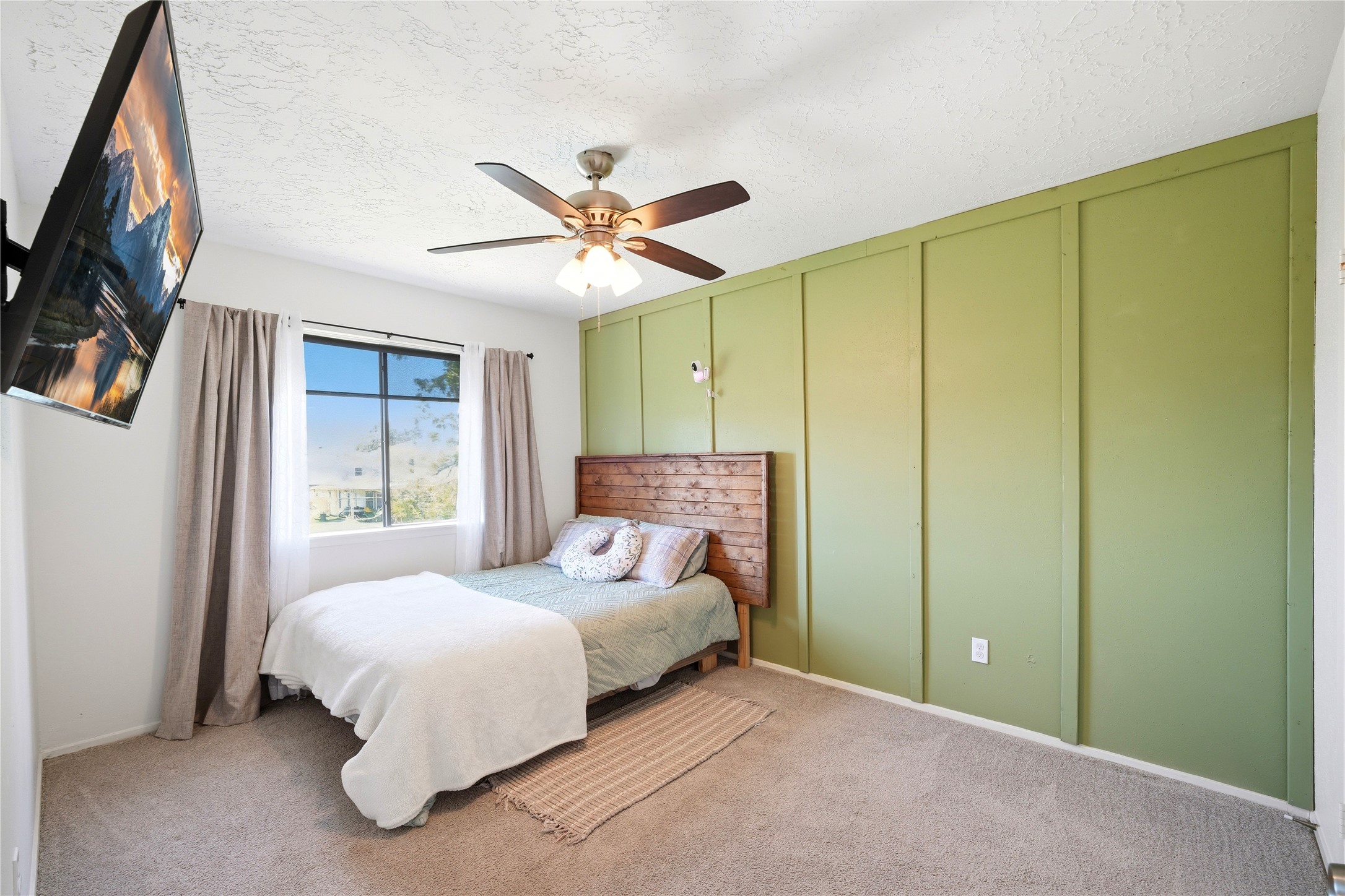 4718 Temple Bell Drive Spring, TX 77388 - Photo 31 of 50 This bedroom features a cozy atmosphere with a soft carpet, a large window for natural light, and a ceiling fan. The accent wall adds character, while the mounted TV offers convenience.