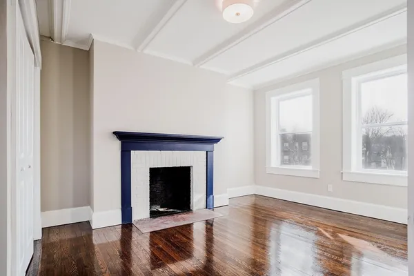 an empty room with wooden floor fireplace and windows