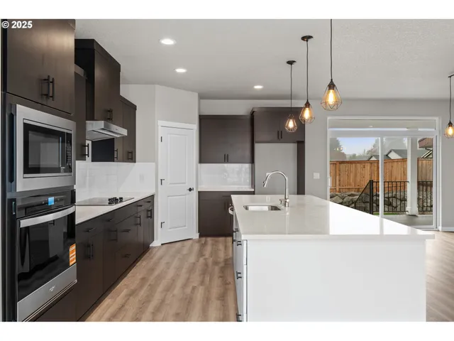 a large white kitchen with a large island oven a stove a refrigerator white cabinets and couches with wooden floor