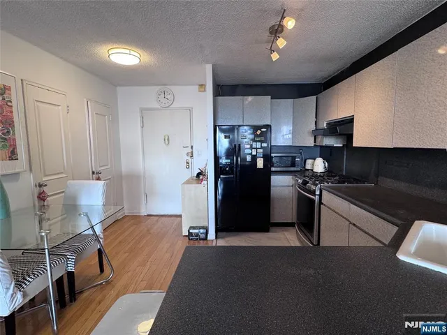 a kitchen with stainless steel appliances kitchen island granite countertop a refrigerator a sink dishwasher a stove and a dining table with wooden floor