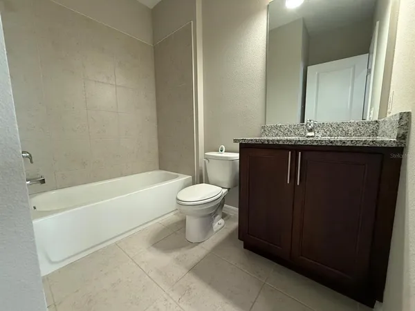a bathroom with a granite countertop bathtub sink vanity mirror and toilet