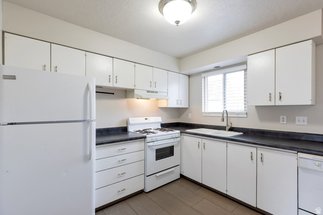 88 West 50 South, Unit J10 Centerville, UT 84014 - Photo 5 of 19 Kitchen featuring white cabinetry, dark countertops, a window with blinds, a white dual-basin sink with a gooseneck faucet, and integrated white appliances including a refrigerator, stove, and dishwasher
