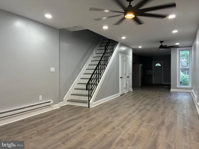a view of an empty room with wooden floor stairs and a ceiling fan