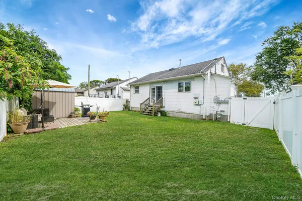 a view of a white house in front of a big yard with potted plants and wooden fence