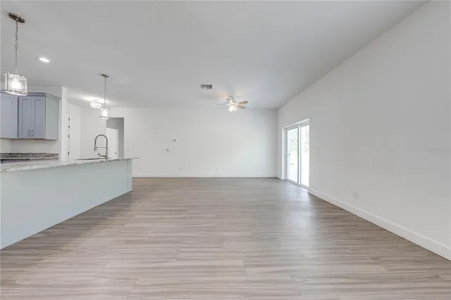 a view of an empty room with kitchen and window