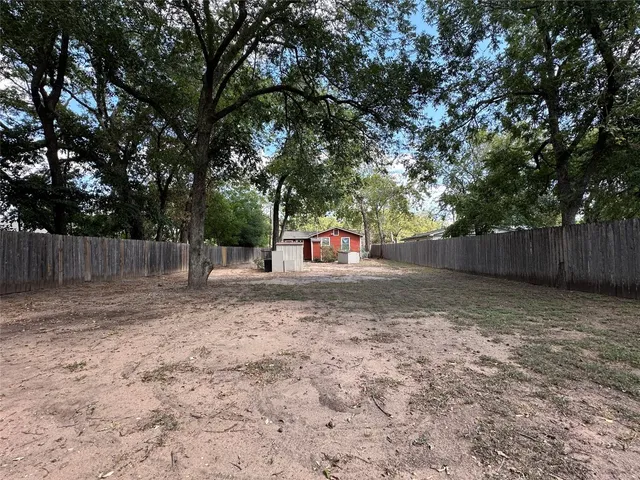 a backyard of a house with large trees and a wooden fence
