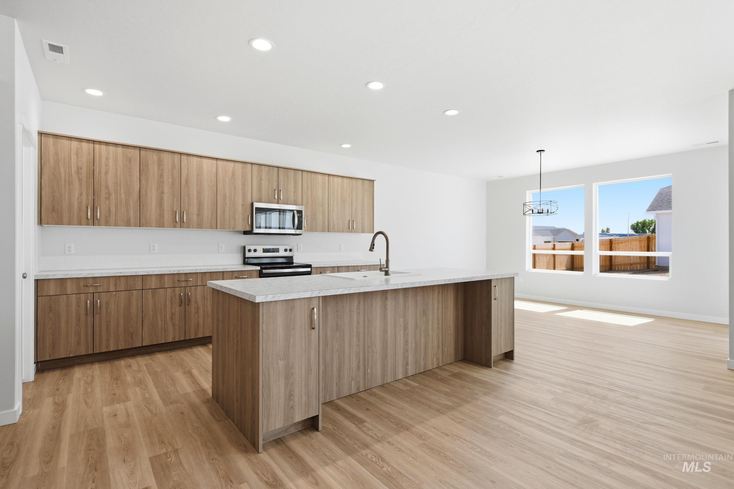13649 Inman Court Caldwell, ID 83607 - Photo 4 of 22 Open-concept kitchen featuring wood-finish cabinetry, a large center island with an integrated sink, and white countertops