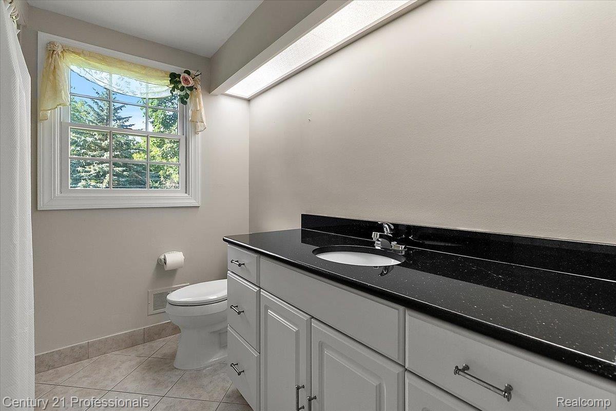 633 Foxhall Road Bloomfield Hills, MI 48304 - Photo 53 of 61 Bathroom featuring a single vanity with a black countertop, white cabinetry, and a window with trim