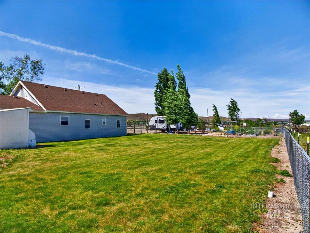 2588 West Sales Yard Road Emmett, ID 83617 - Photo 34 of 49 Expansive grassy yard area bordered by chain-link fencing, with a light blue siding structure featuring multiple windows and a brown shingle roof