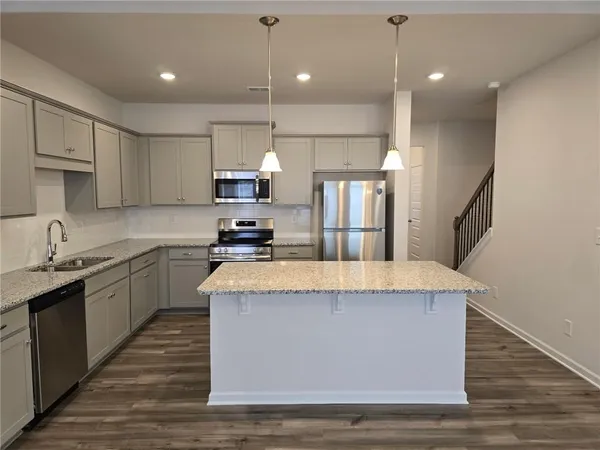 a large kitchen with stainless steel appliances kitchen island granite countertop a stove a sink a refrigerator and white cabinets with wooden floor