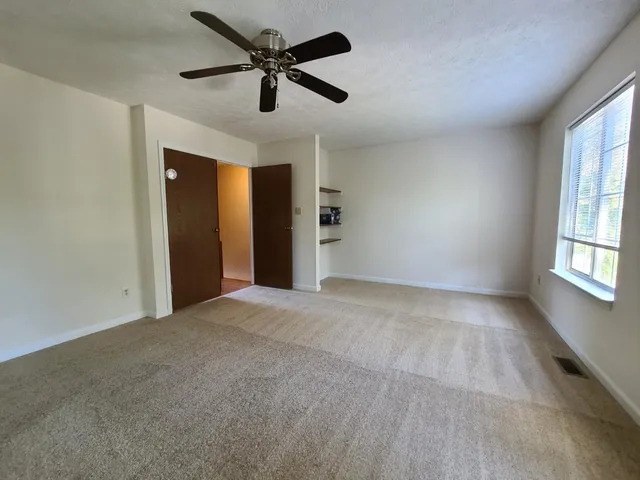 an empty room with chandelier fan and windows