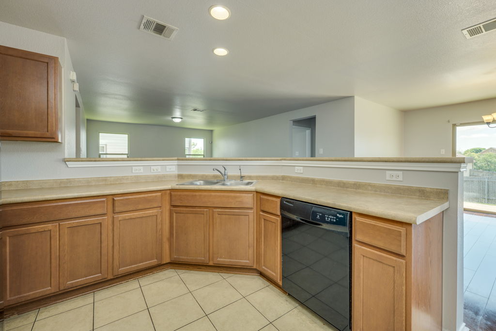 210 Cushman Drive Kyle, TX 78640 - Photo 10 of 21 Kitchen featuring wood-finish cabinetry, a double basin sink, a black dishwasher, and tile flooring