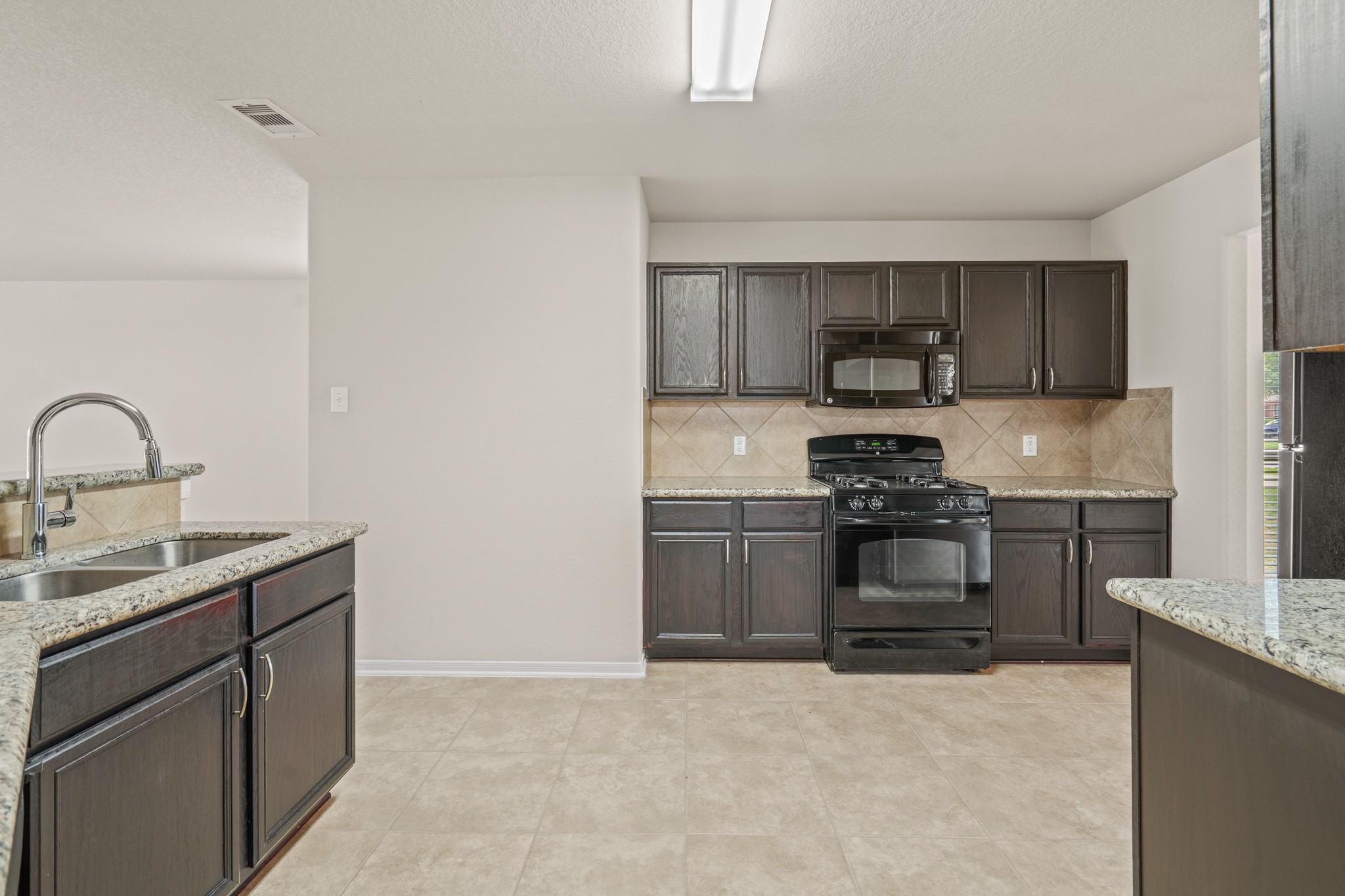 3118 Winchester Rnch Trail Katy, TX 77493 - Photo 6 of 22 A focused view of the kitchen's cooking zone highlights rich dark espresso cabinetry, granite countertops, a gas range, built-in microwave, diagonal tile backsplash, and generous counter space — everything a family needs to cook, gather, and create lasting memories together.