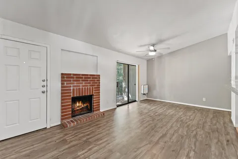 a view of an empty room with wooden floor fireplace and a window