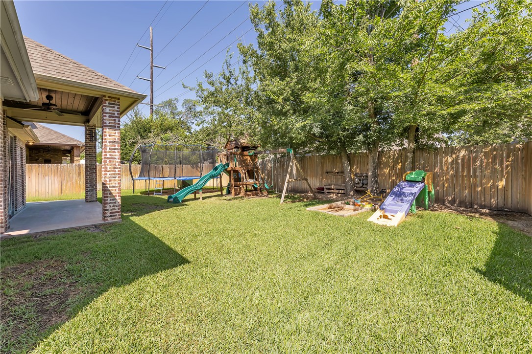 8312 Raintree Drive College Station, TX 77845 - Photo 28 of 30 Expansive backyard featuring a covered patio with brick columns and a ceiling fan, mature trees, a wooden privacy fence, and a manicured lawn
