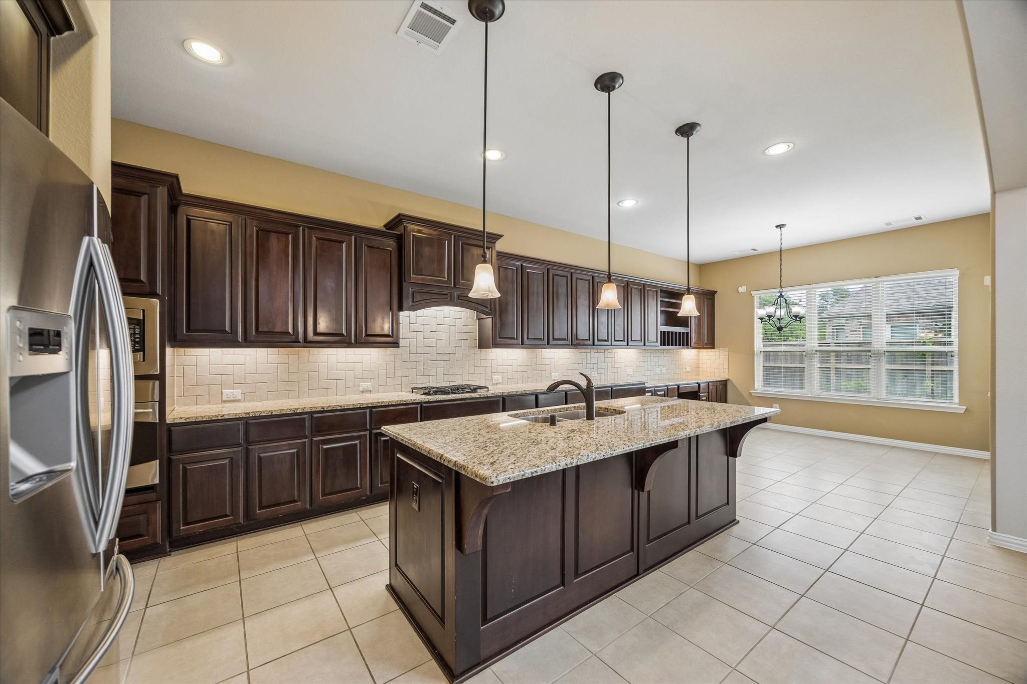 17403 Astrachan Road Richmond, TX 77407 - Photo 8 of 40 Spacious kitchen with dark wood cabinets, granite countertops, and a large island. Features stainless steel appliances, tile flooring, and ample natural light from large windows. Ideal for cooking and entertaining.