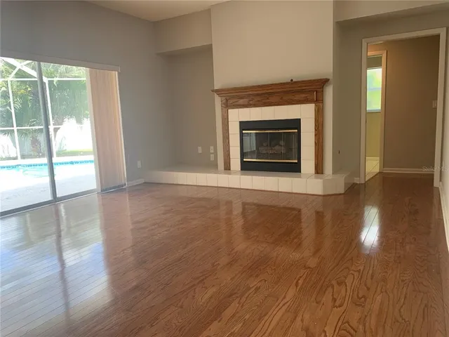 an empty room with wooden floor fireplace and windows