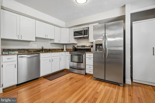a kitchen with stainless steel appliances granite countertop a refrigerator a sink a stove and white cabinets