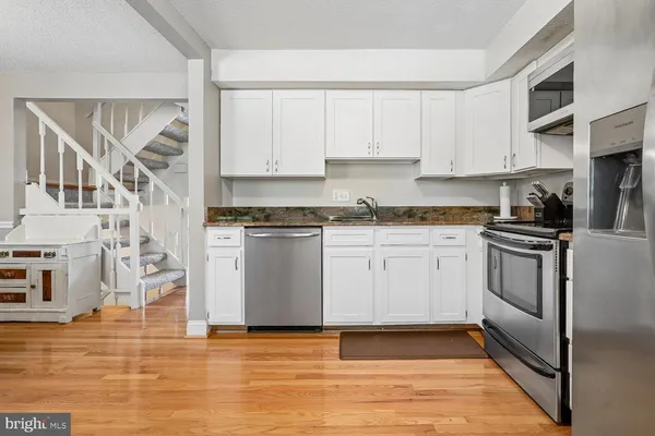 a kitchen with stainless steel appliances granite countertop a refrigerator a stove top oven a sink and dishwasher with wooden floor