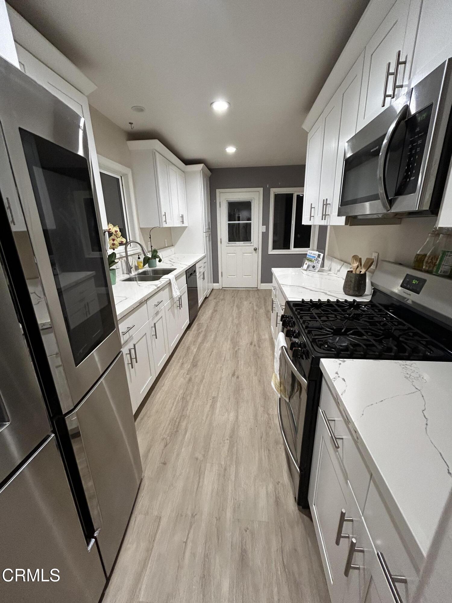 3651 South E Street Oxnard, CA 93033 - Photo 23 of 31 a large kitchen with stainless steel appliances granite countertop a stove a sink dishwasher a microwave oven and a refrigerator with wooden floor