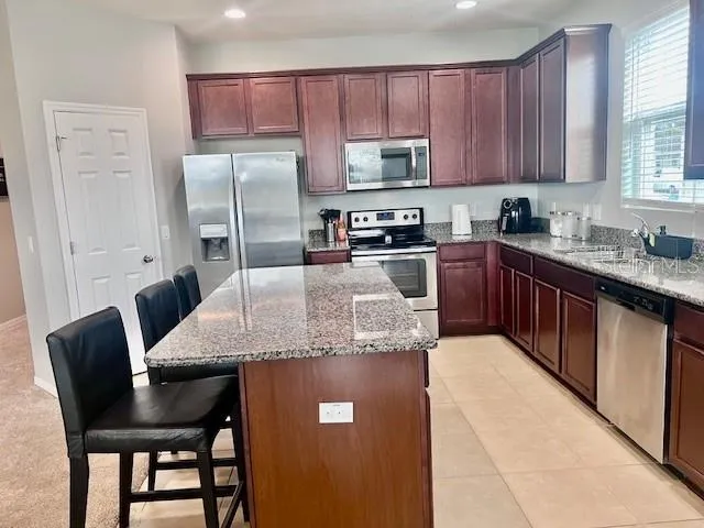 a kitchen with stainless steel appliances granite countertop a table chairs refrigerator and sink