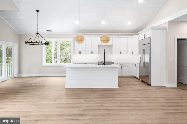 a large kitchen with stainless steel appliances kitchen island granite countertop a refrigerator a stove and white cabinets with wooden floor