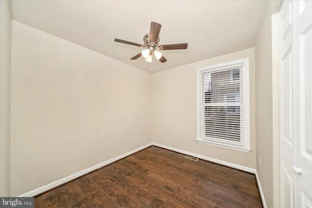 an empty room with wooden floor ceiling fan and windows
