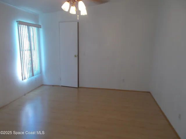 an empty room with window fan and wooden floor
