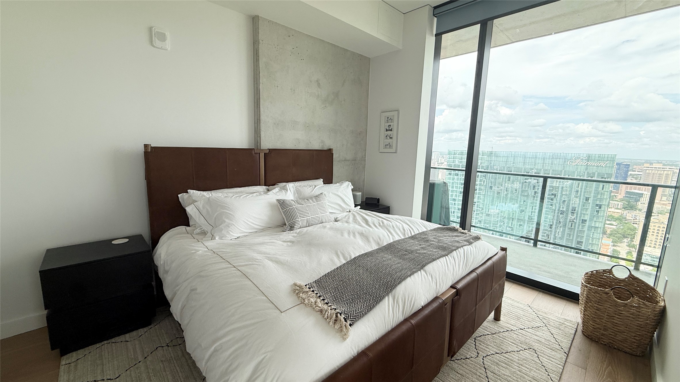 610 Davis Street, Unit 4007 Austin, TX 78701 - Photo 6 of 29 This bedroom features large floor-to-ceiling windows, a concrete accent wall, and a brown leather bed frame