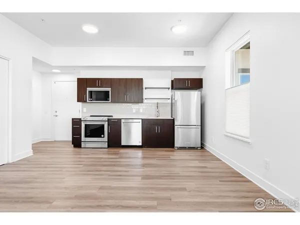 a view of a kitchen with stainless steel appliances wooden floor and chair