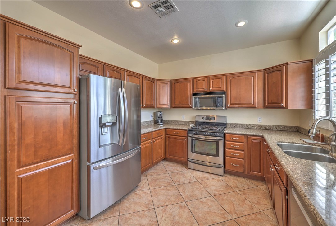 8325 Alta Drive Las Vegas, NV 89145 - Photo 11 of 31 Kitchen with stainless steel appliances, Granite countertops, brown cabinets, light tile patterned floors, and recessed lighting