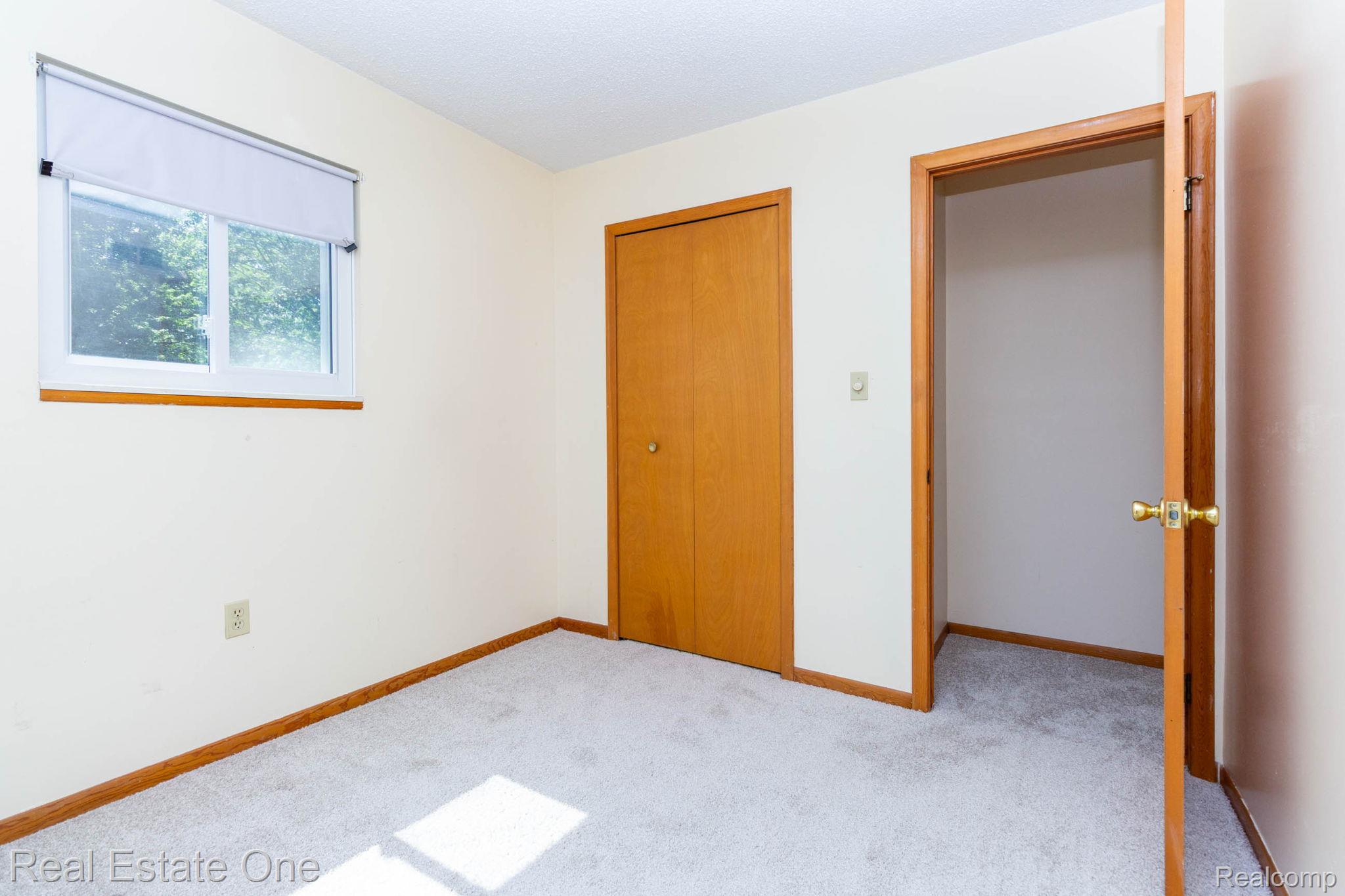 13912 Clinton River Road Sterling Heights, MI 48313 - Photo 18 of 43 Carpeted interior room featuring a window with a white frame and roller shade, an adjacent wood-paneled closet, and wood trim detailing throughout