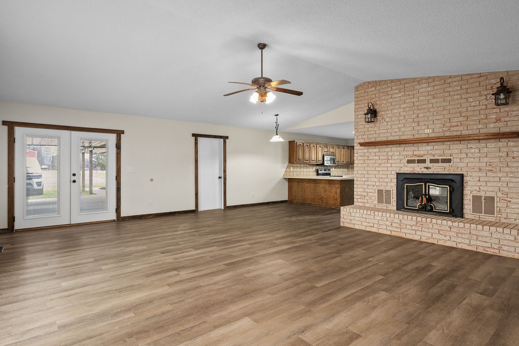  Living room with a fireplace, lofted ceiling, dark wood-style floors, a ceiling fan, and french doors