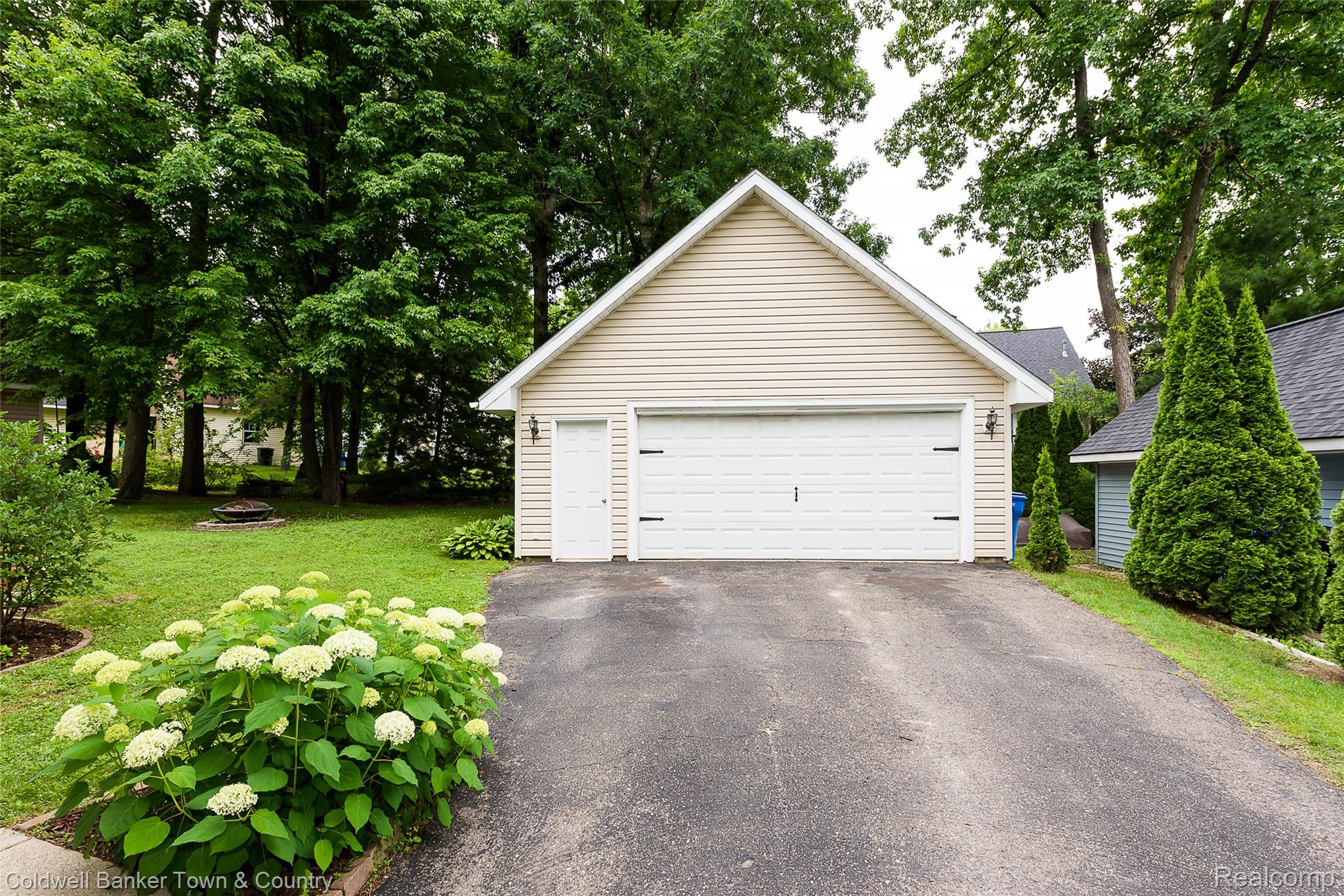 411 Springwell Lane Howell, MI 48843 - Photo 32 of 33 Detached two-car garage with light-colored horizontal siding, a white garage door, and an exterior side door