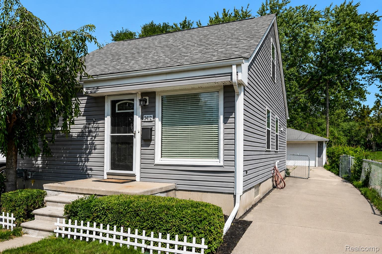 Gray siding exterior with white trim, concrete steps leading to the entrance, a paved driveway, and a detached garage structure