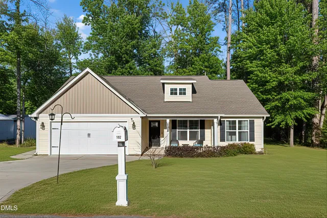 a view of a yard in front of a house with plants and large tree