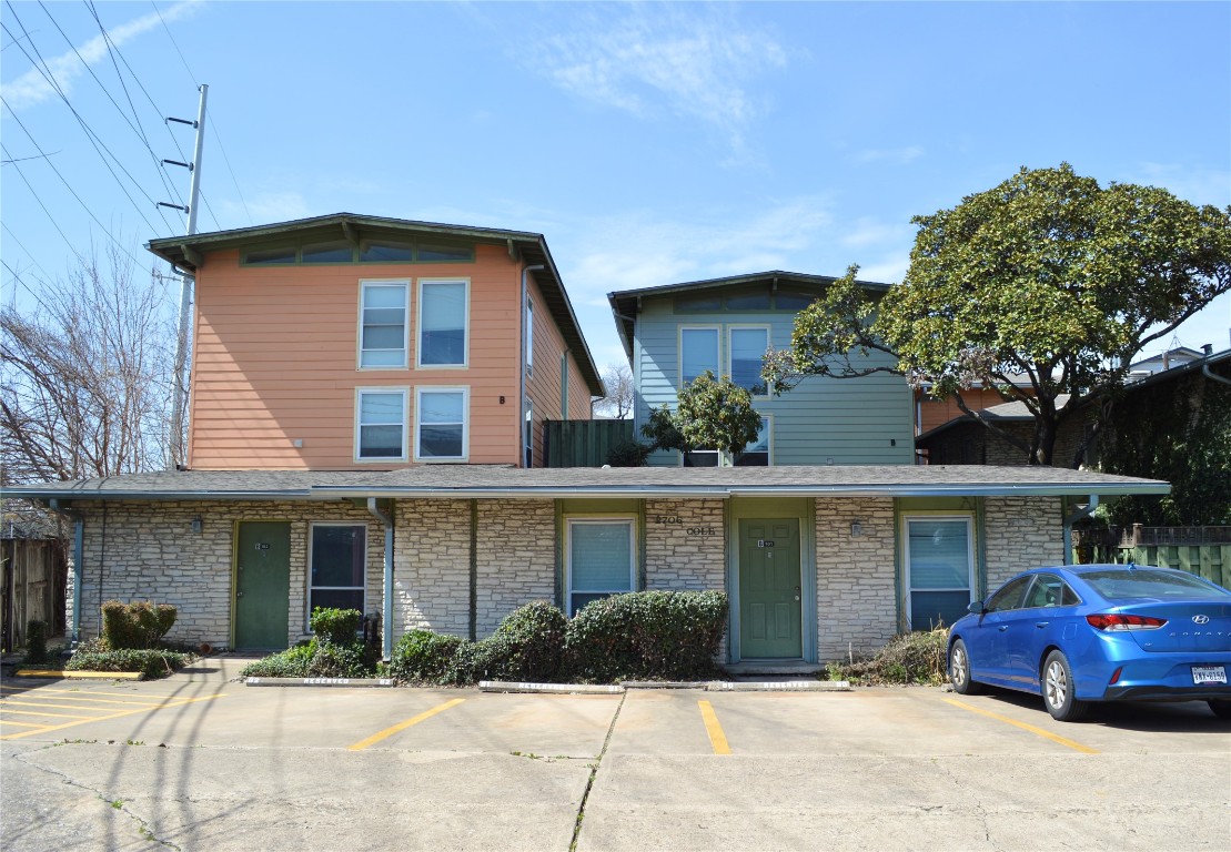 View of front facade featuring uncovered parking, stone siding, and fence